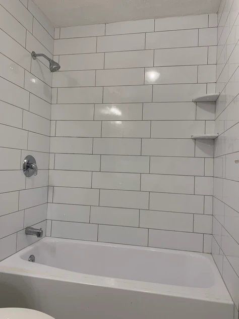 A bathroom with white tile walls and a bathtub.