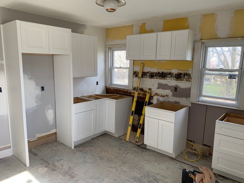 A kitchen under construction with white cabinets and a yellow ladder.