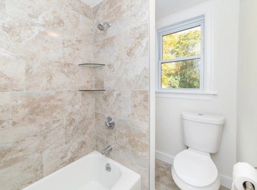 A bathroom with a tub, toilet, shower and window.