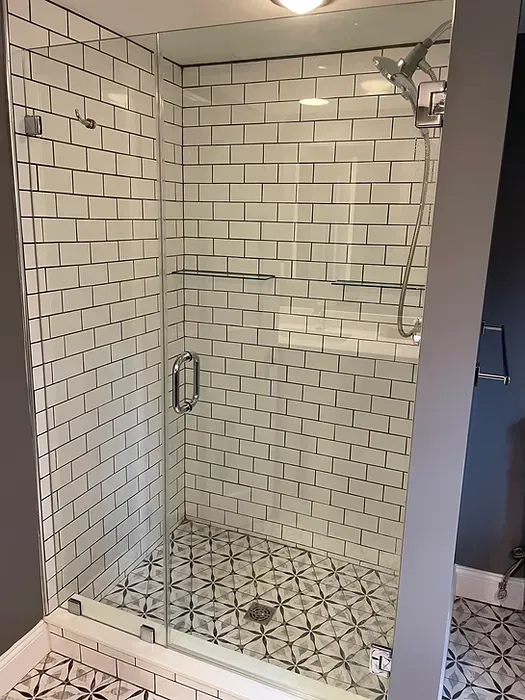 A bathroom with white brick walls and a walk in shower with a glass door.