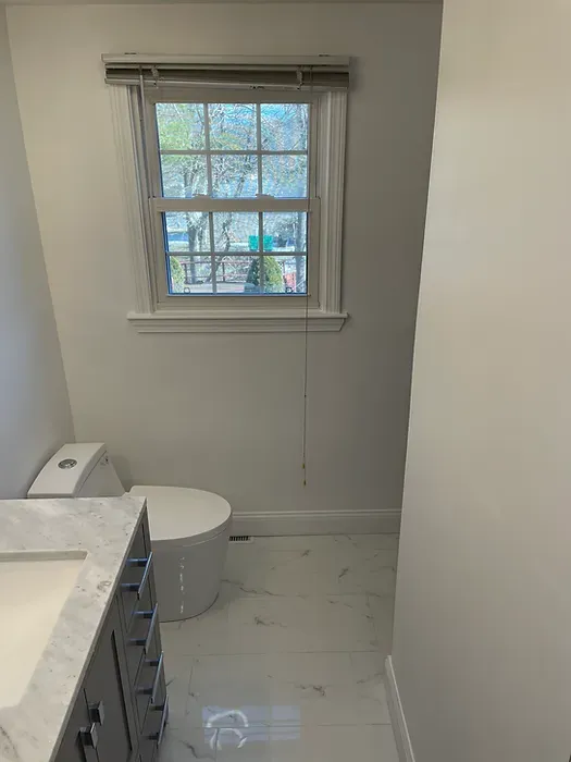 A bathroom with a toilet , sink , and window.