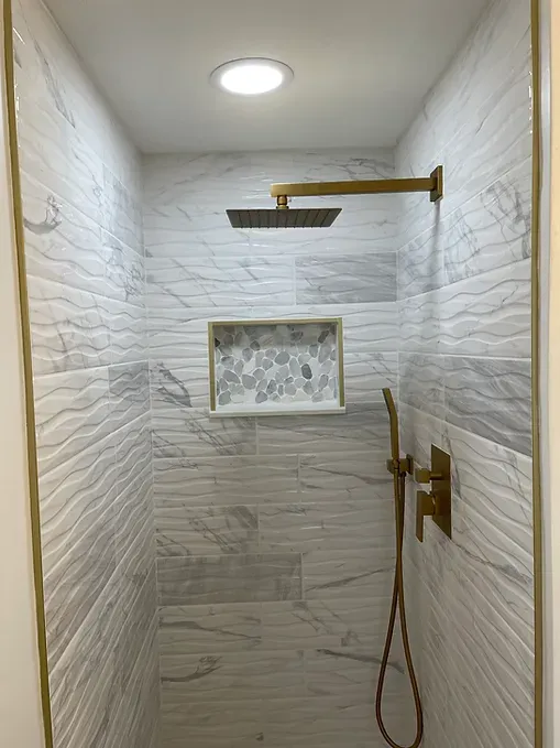 A shower with a marble wall and a gold shower head.