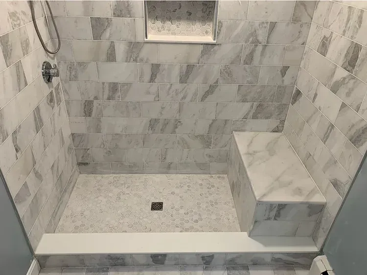 A shower with a bench and a shower head in a bathroom.