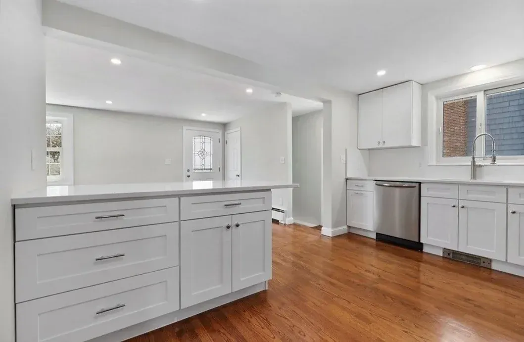 An empty kitchen with white cabinets and hardwood floors.