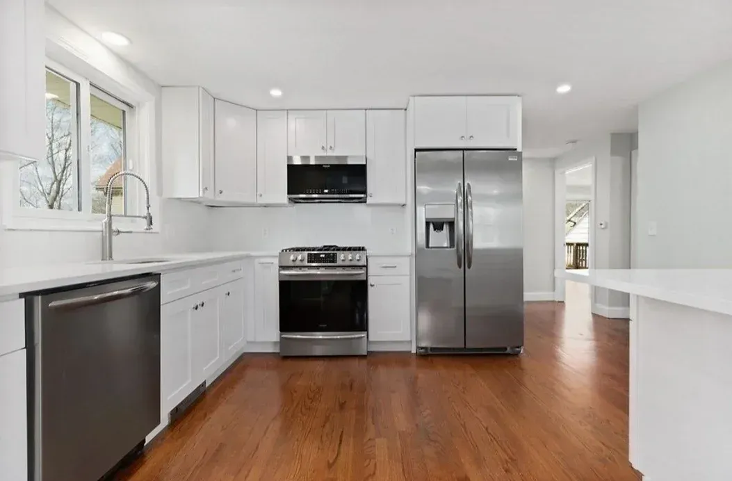 A kitchen with white cabinets , stainless steel appliances , and hardwood floors.
