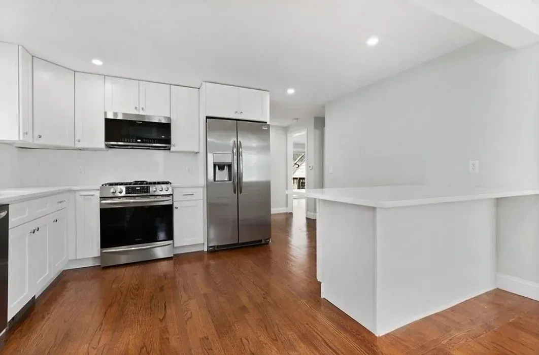 A kitchen with white cabinets , stainless steel appliances , and hardwood floors.