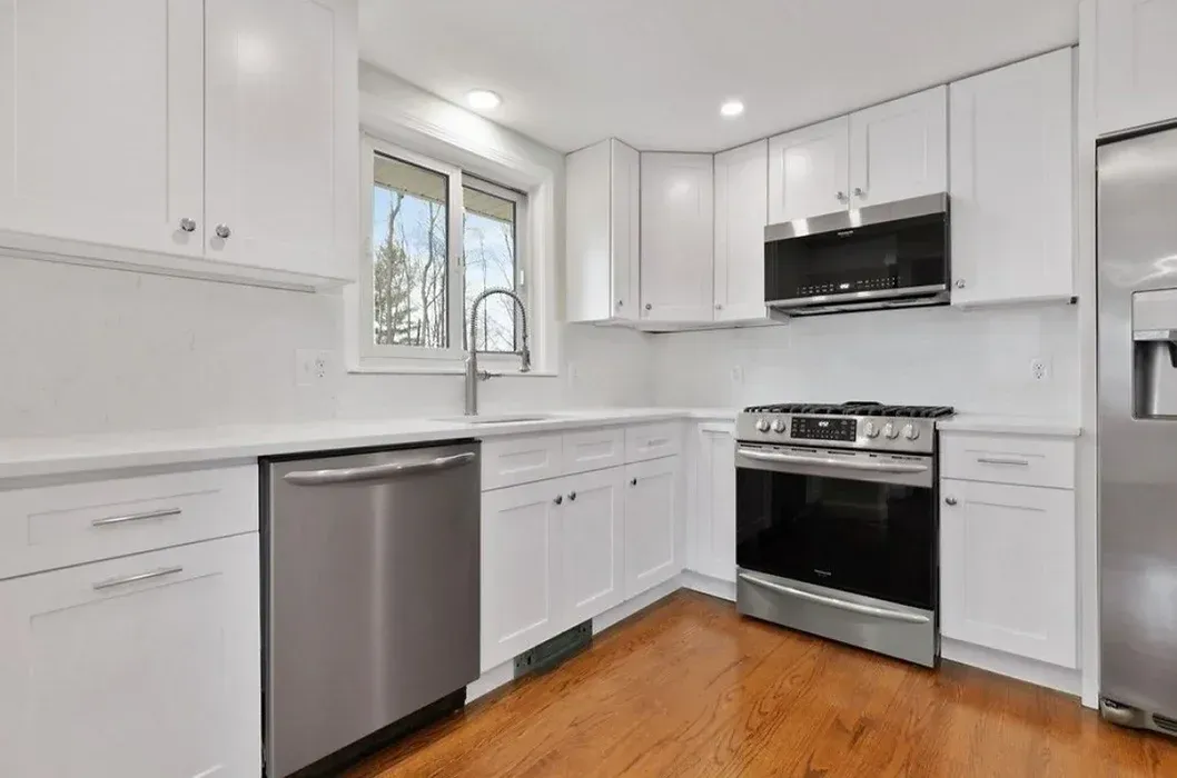 A kitchen with white cabinets , stainless steel appliances , and hardwood floors.