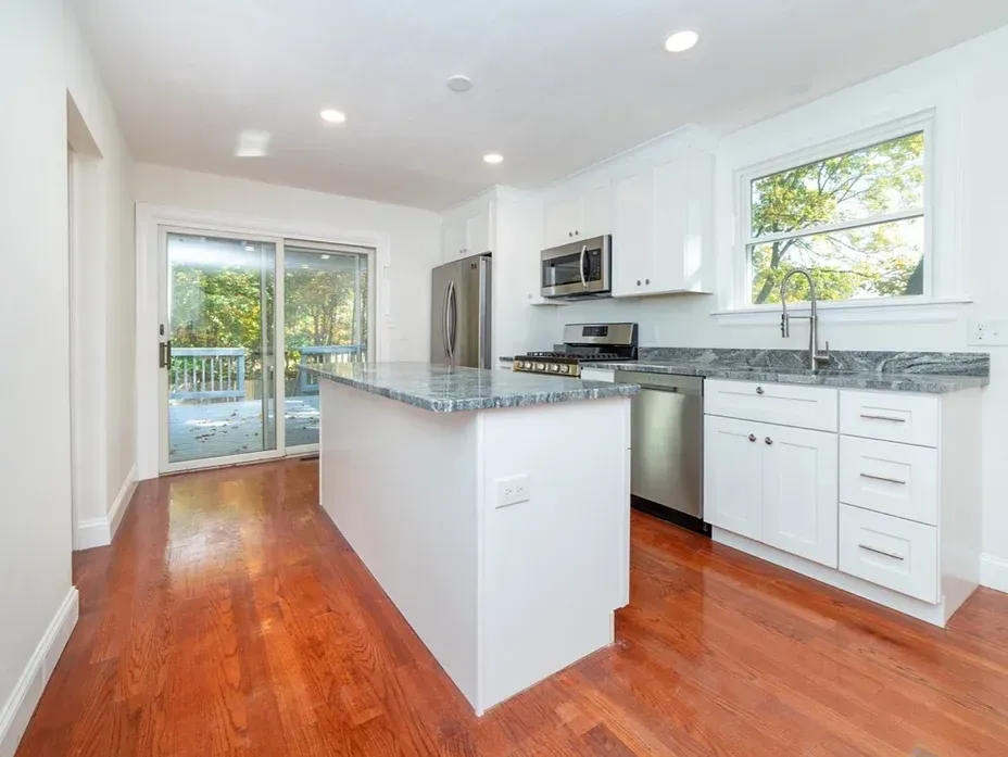 A kitchen with white cabinets , granite counter tops , stainless steel appliances and hardwood floors.