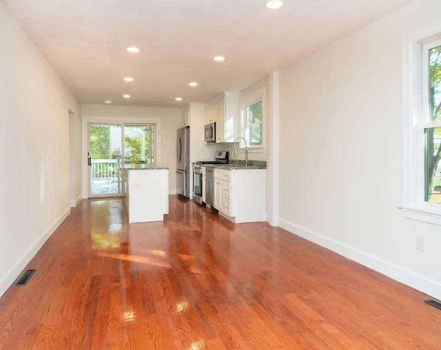 An empty living room with hardwood floors and a kitchen.