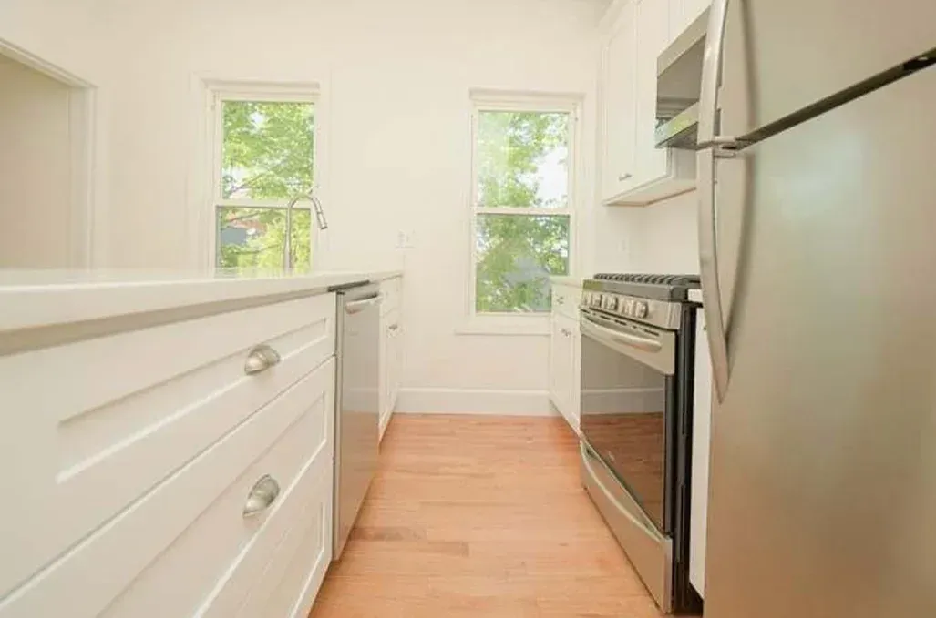 A kitchen with white cabinets , stainless steel appliances , and hardwood floors.