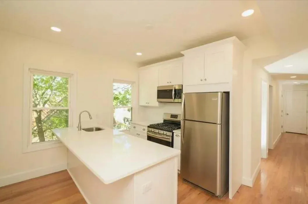 A kitchen with white cabinets , a stainless steel refrigerator , a stove and a microwave.