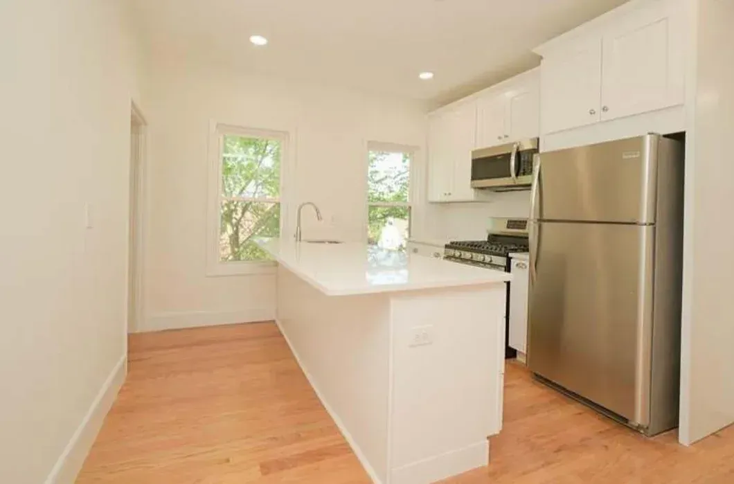A kitchen with white cabinets , a stainless steel refrigerator , a stove , and a sink.