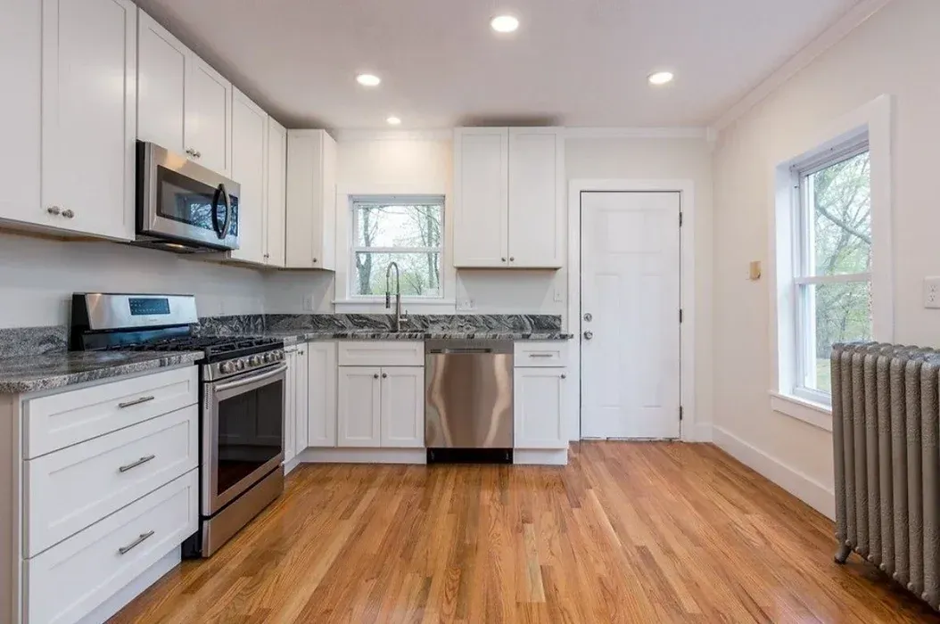 A kitchen with white cabinets , stainless steel appliances , and hardwood floors.