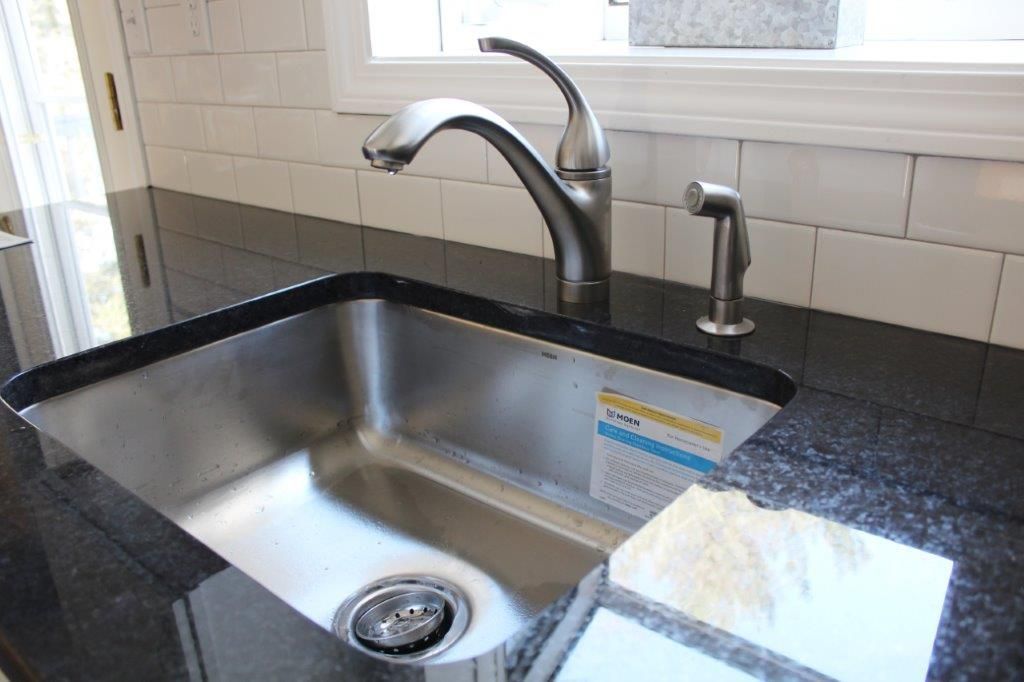 An attractive stainless steel kitchen sink with a black countertop