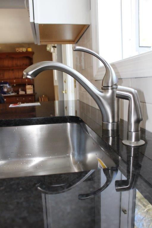 A lovely stainless steel kitchen sink with a black countertop