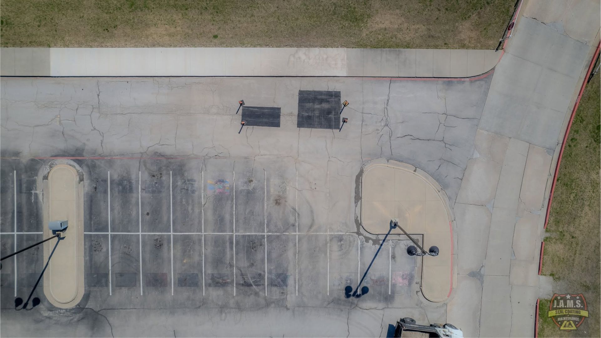 Aerial view of a concrete parking lot with painted lines, light poles, and grassy edges
