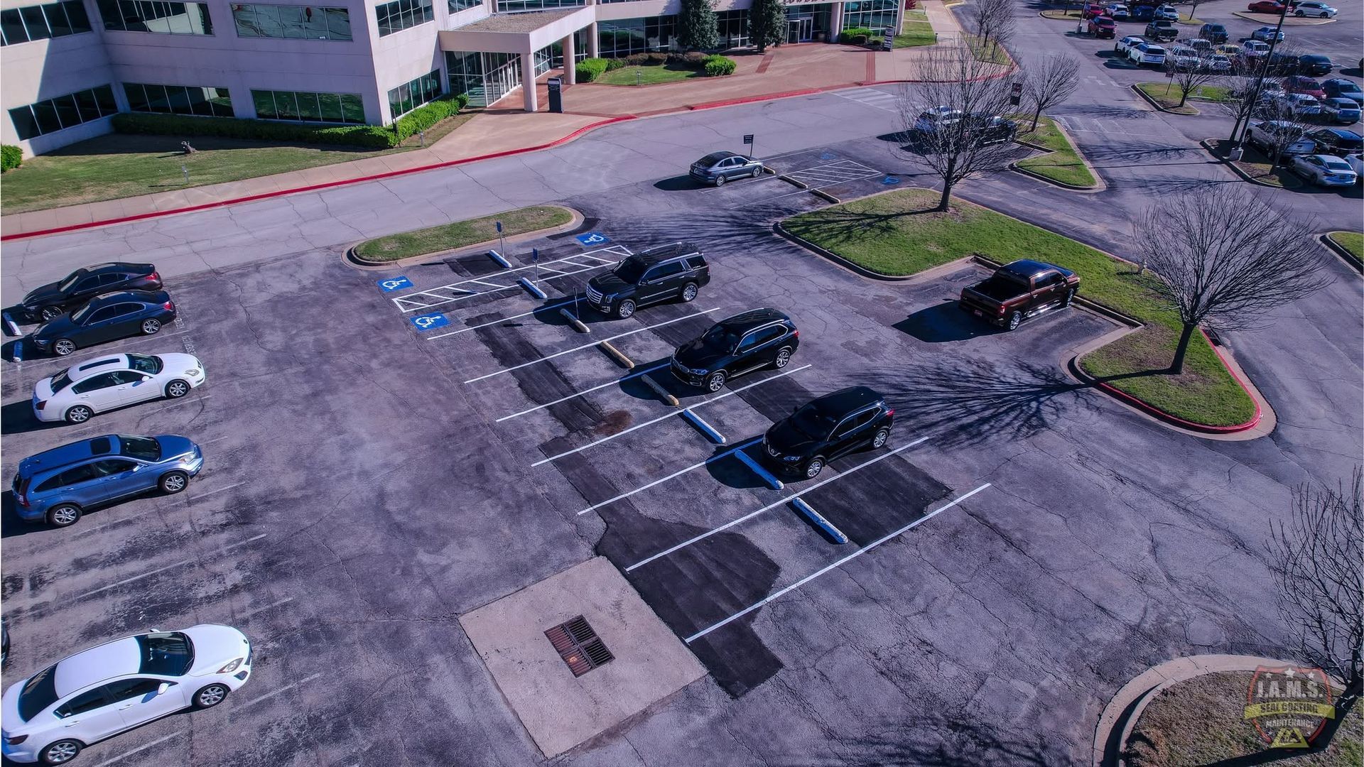 Aerial view of a mostly empty parking lot beside a building, with several parked cars and painted spaces.