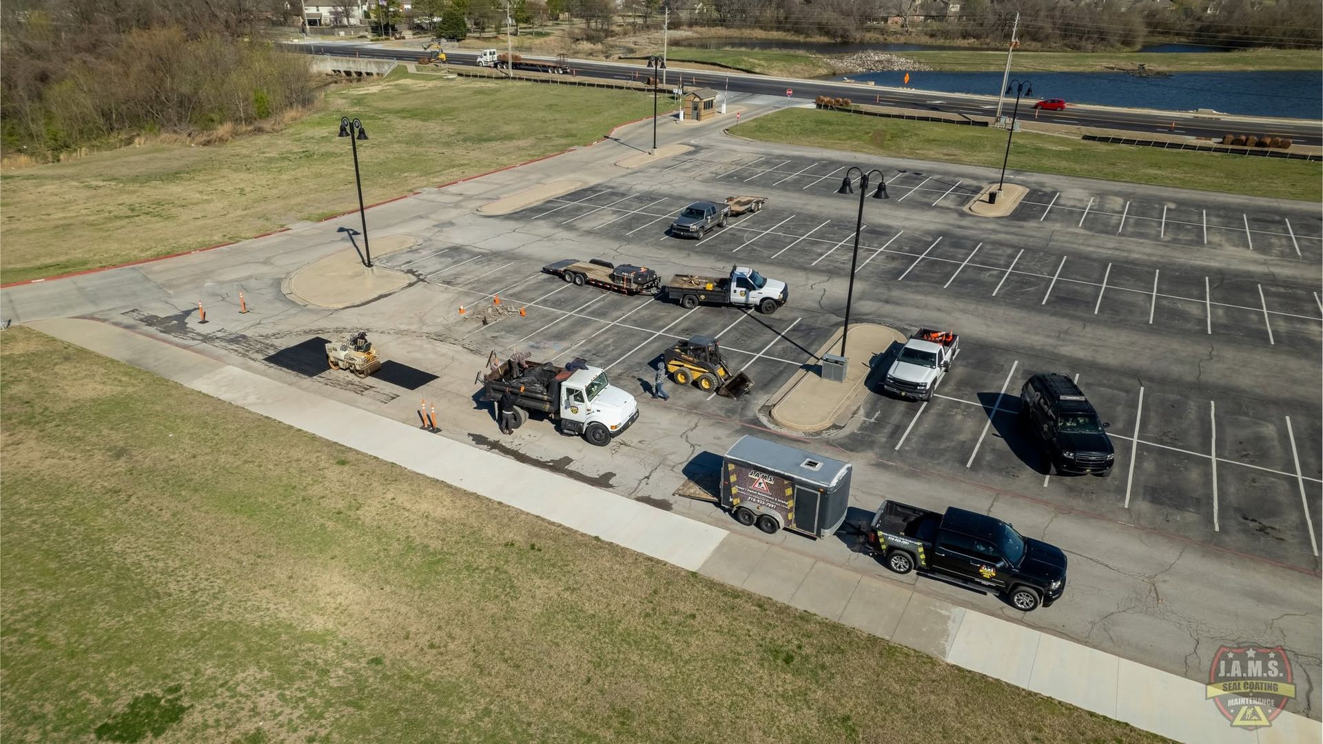 Aerial view of a mostly empty parking lot with several parked cars and a grassy field nearby.