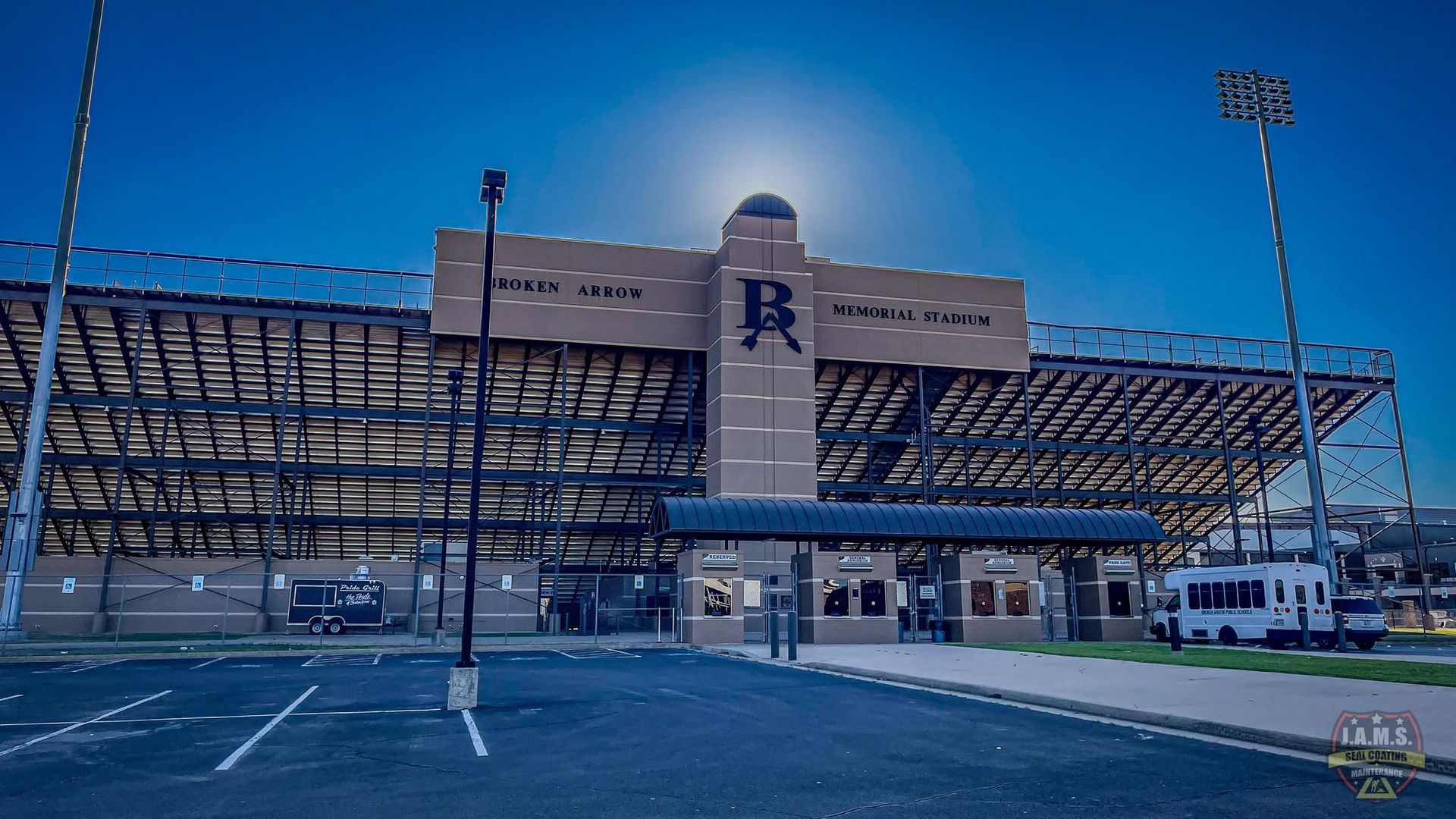 Modern stadium exterior with a large blue “R” on the facade and parking lot in front