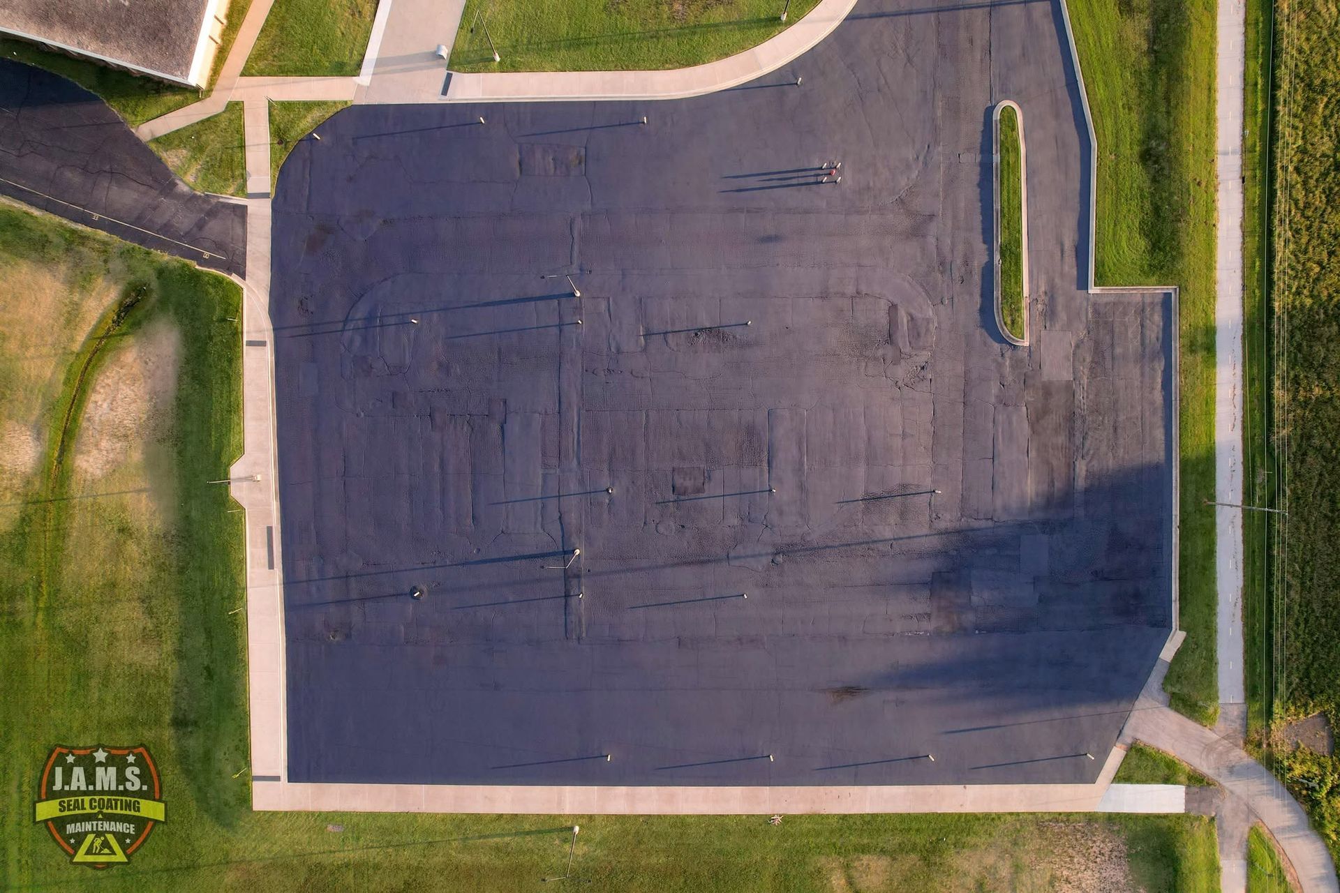 Aerial view of an empty paved parking lot bordered by grass and sidewalks.
