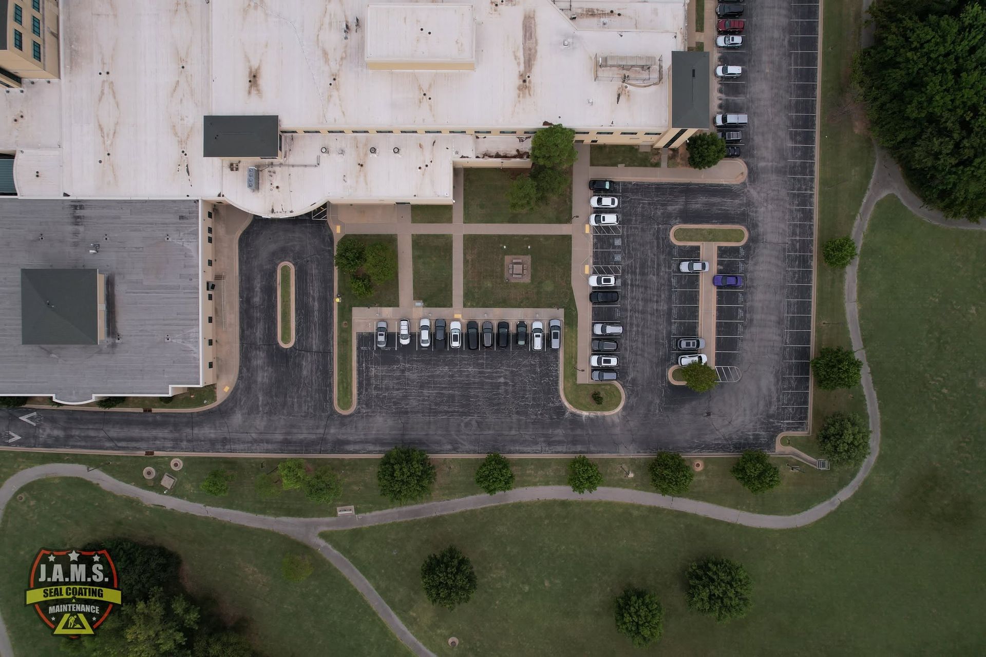 Aerial view of a parking lot beside a building, with a few parked cars and grassy areas nearby.