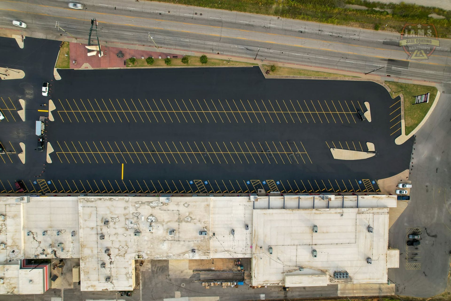 Aerial view of a mostly empty parking lot beside a road and concrete building.