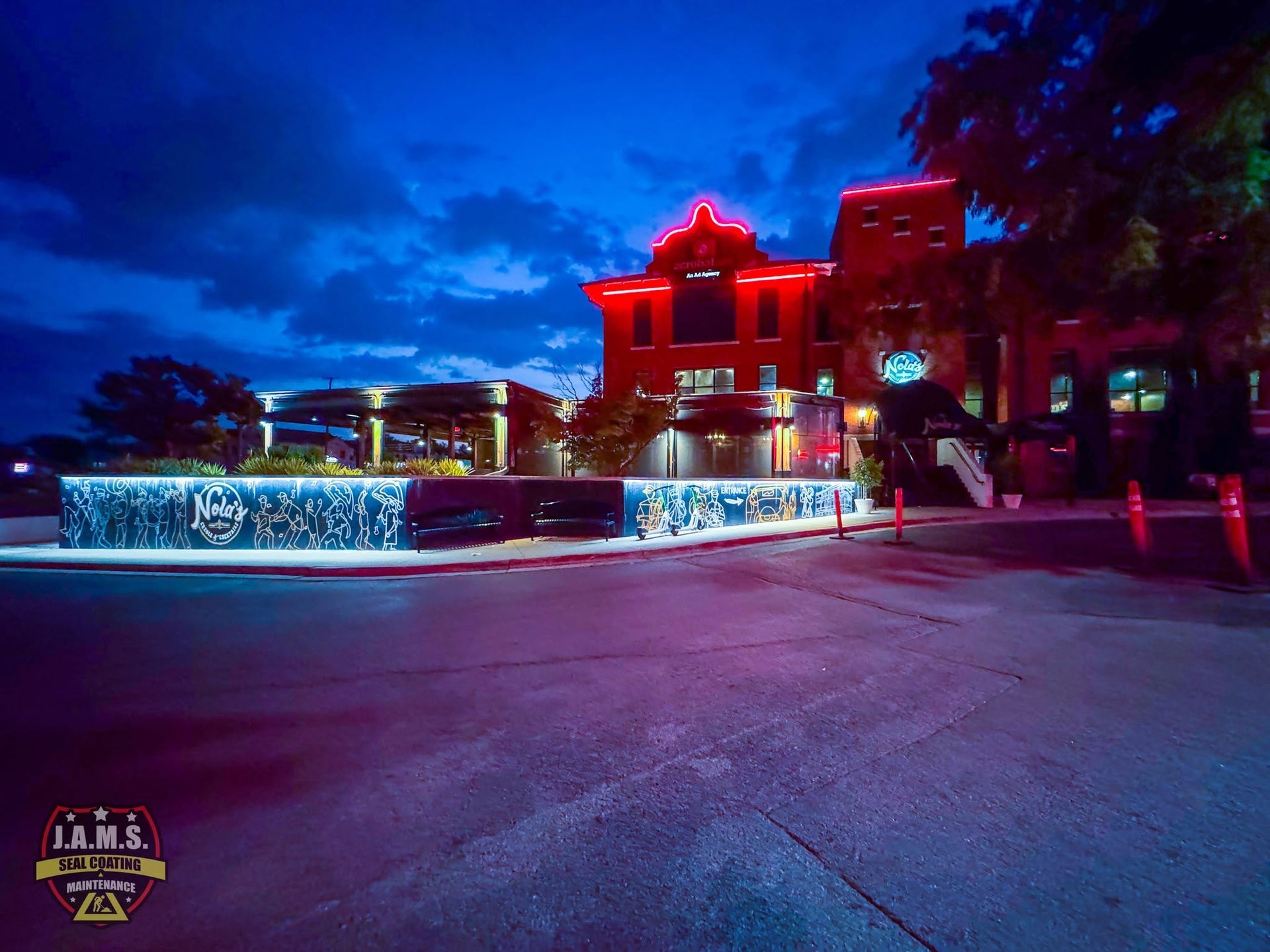 Night view of a red-lit building with a glowing blue-lit fountain in front under a dark blue sky