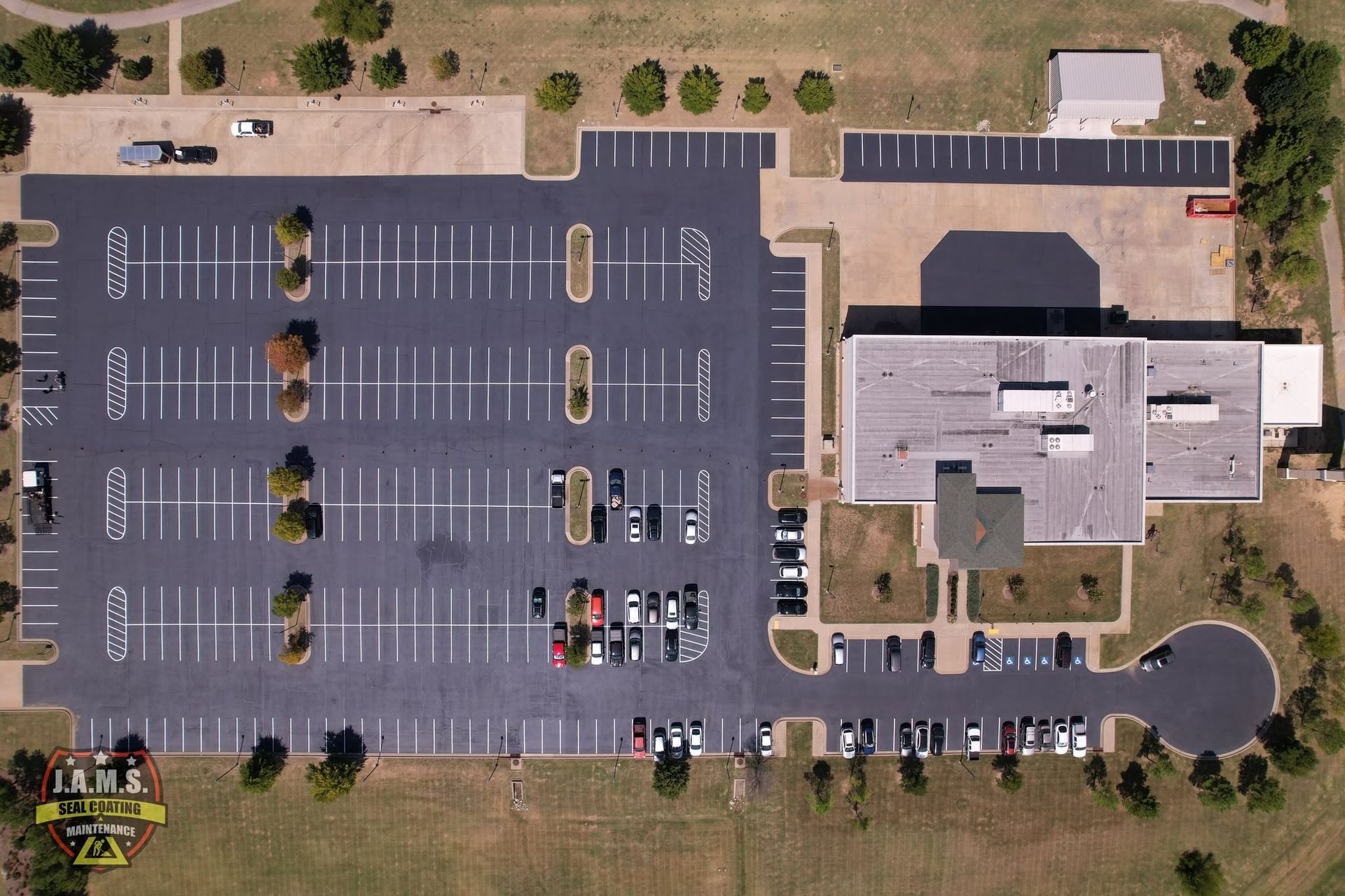 Aerial view of a school building and mostly empty parking lot with painted parking spaces and a few cars.