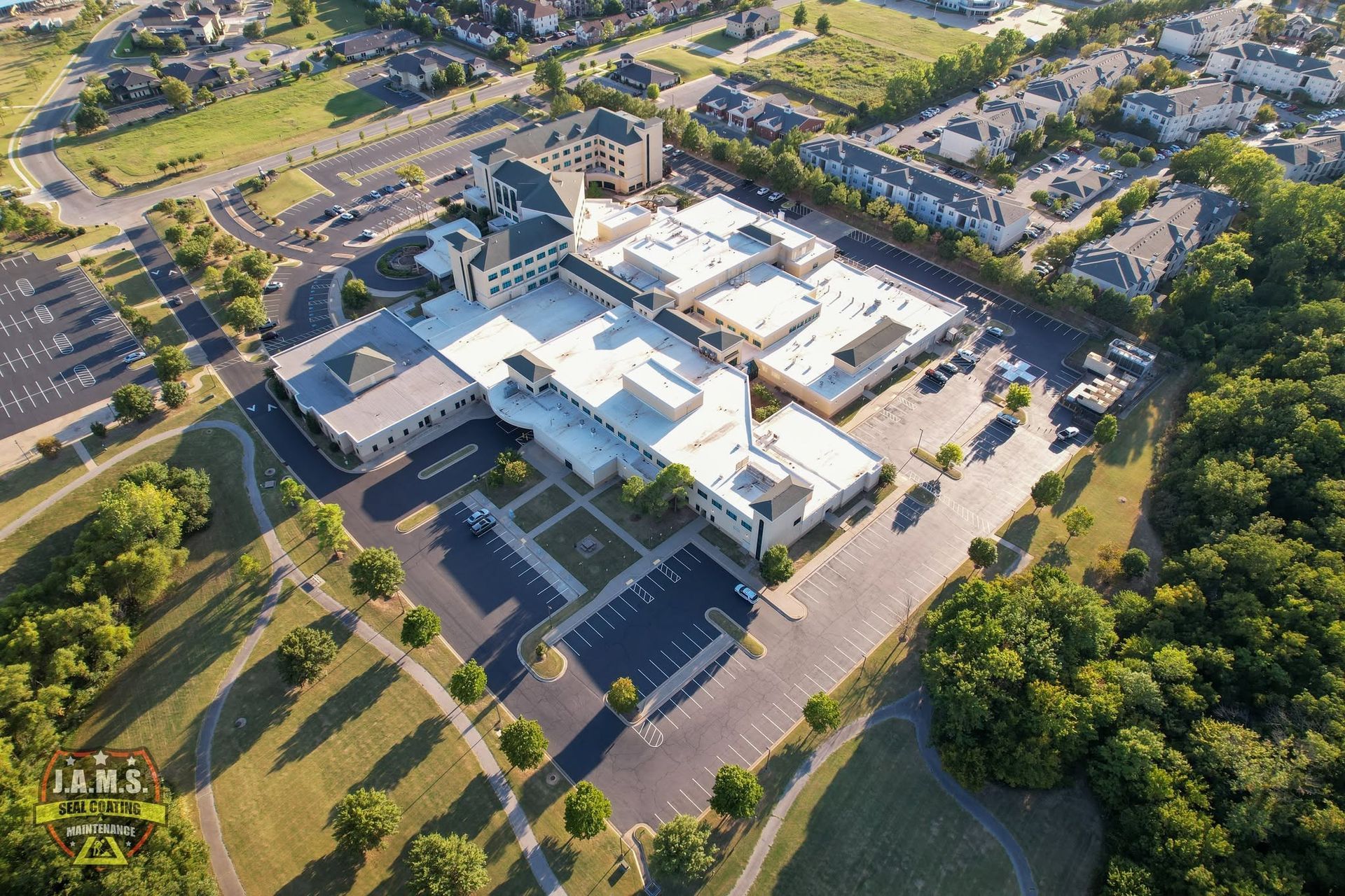 Aerial view of a large school campus with white-roofed buildings, parking lots, and trees.