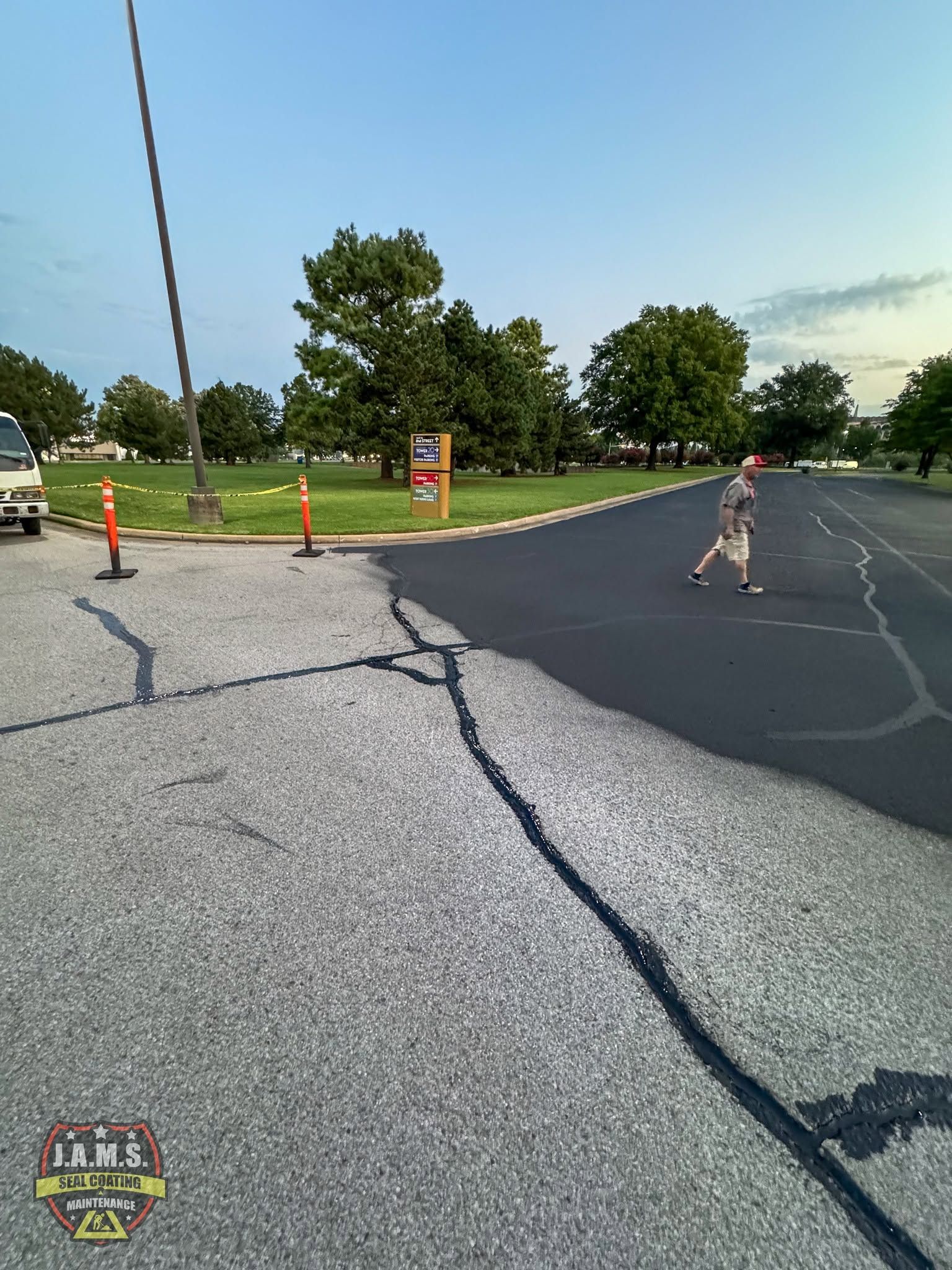 Cracked asphalt lot with orange cones, trees, and a person walking near the right side.
