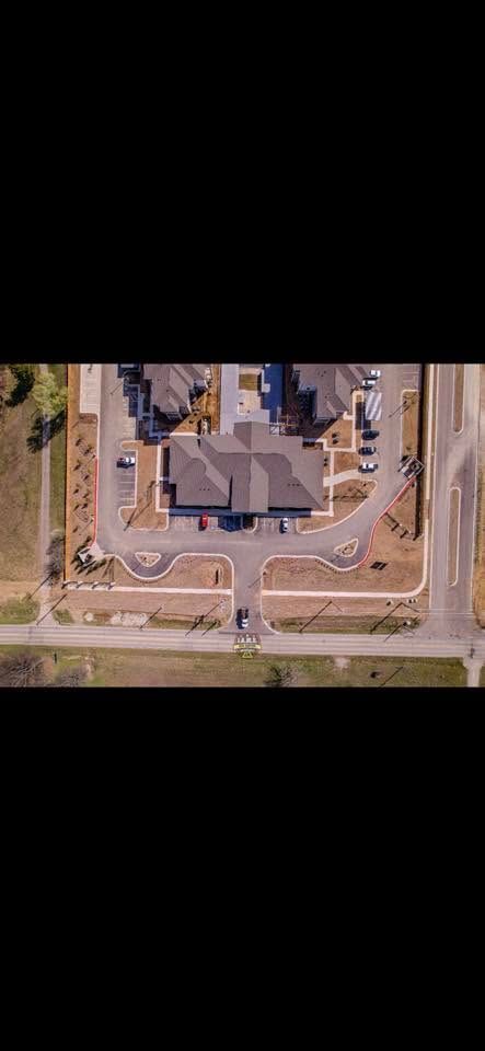 Aerial view of a beige house with a circular driveway and parked cars in a suburban neighborhood.