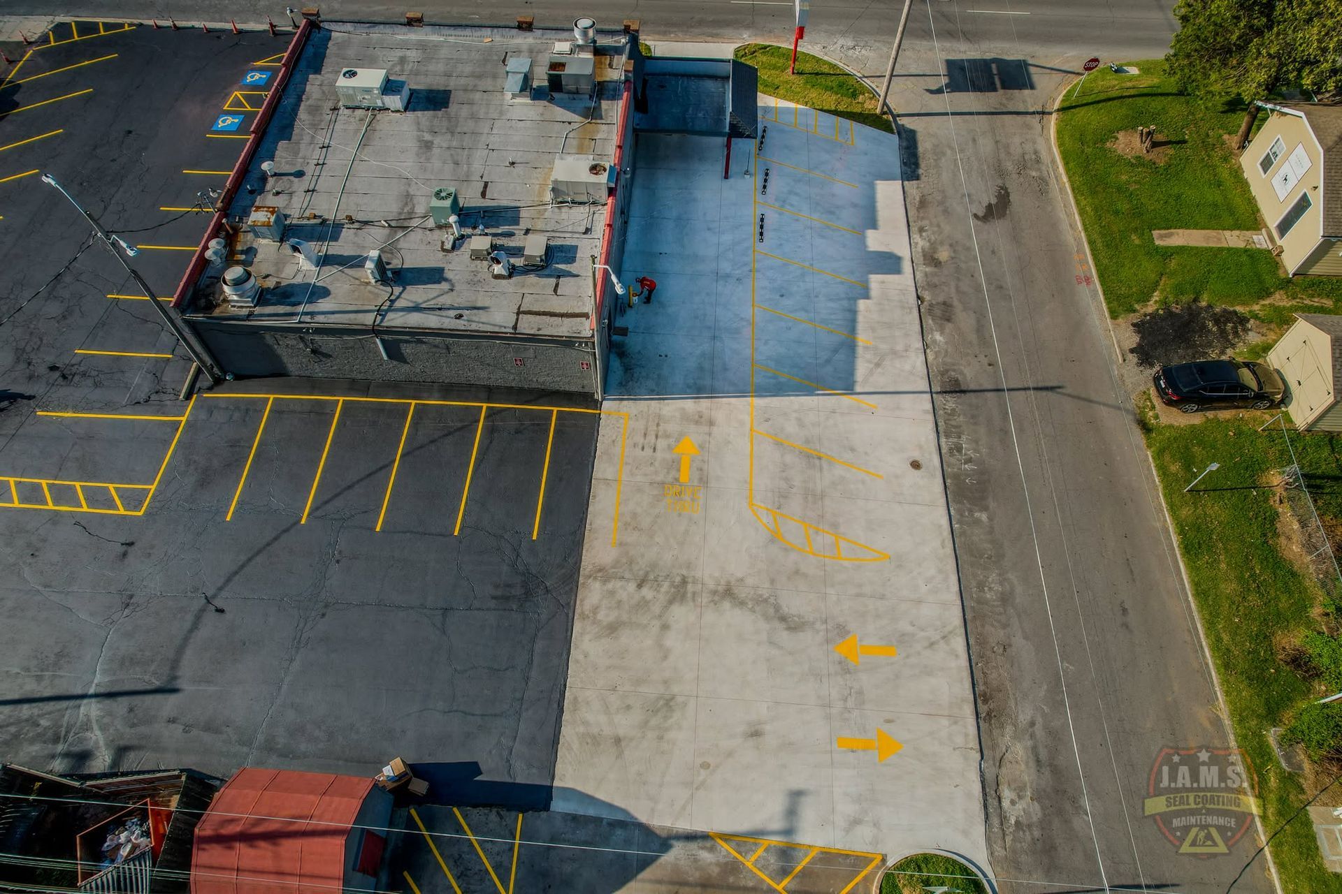 Aerial view of a parking lot beside a flat-roofed building, with blue and gray paving and painted parking lines.