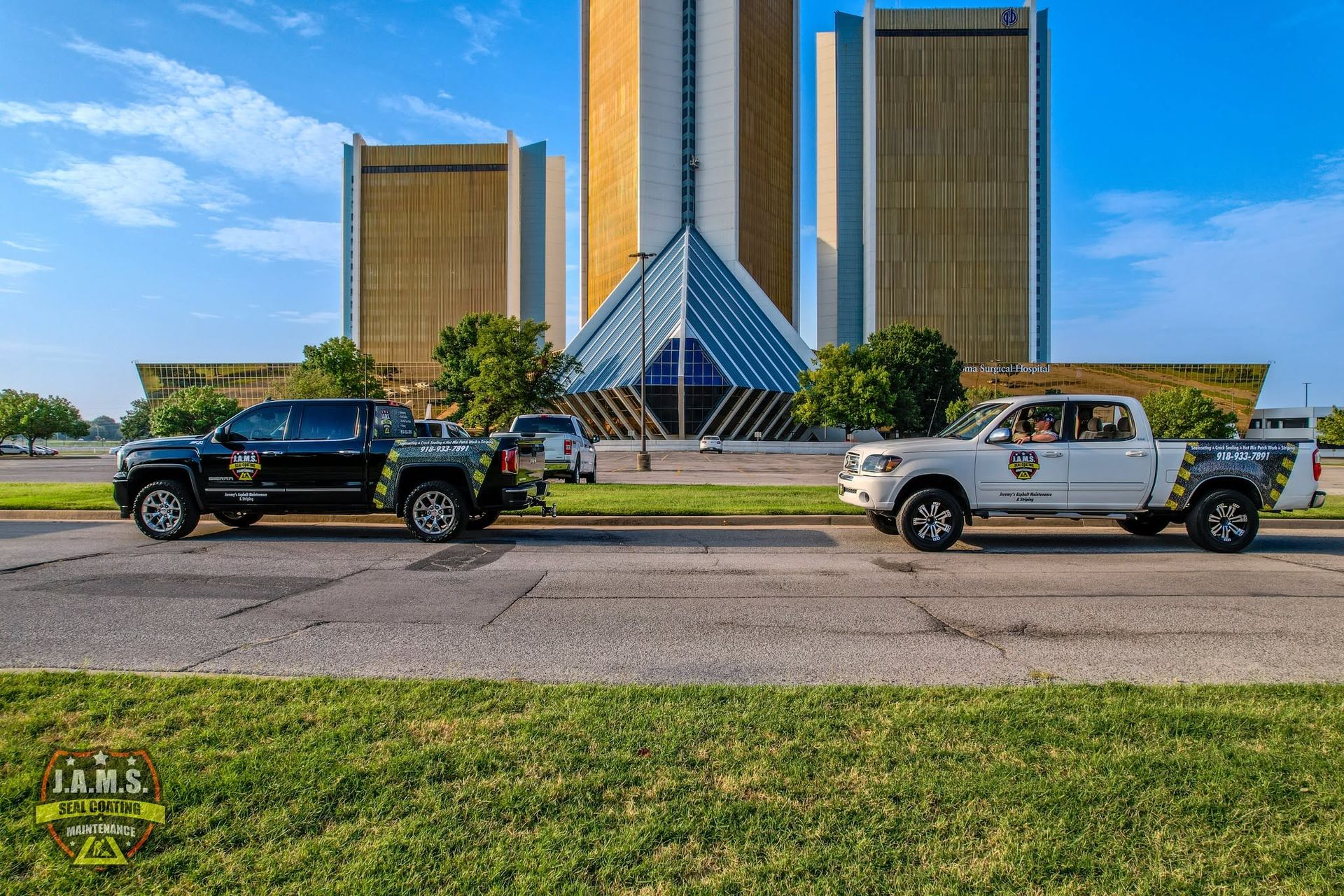 Two pickup trucks parked before a modern building with a glass pyramid entrance under a blue sky