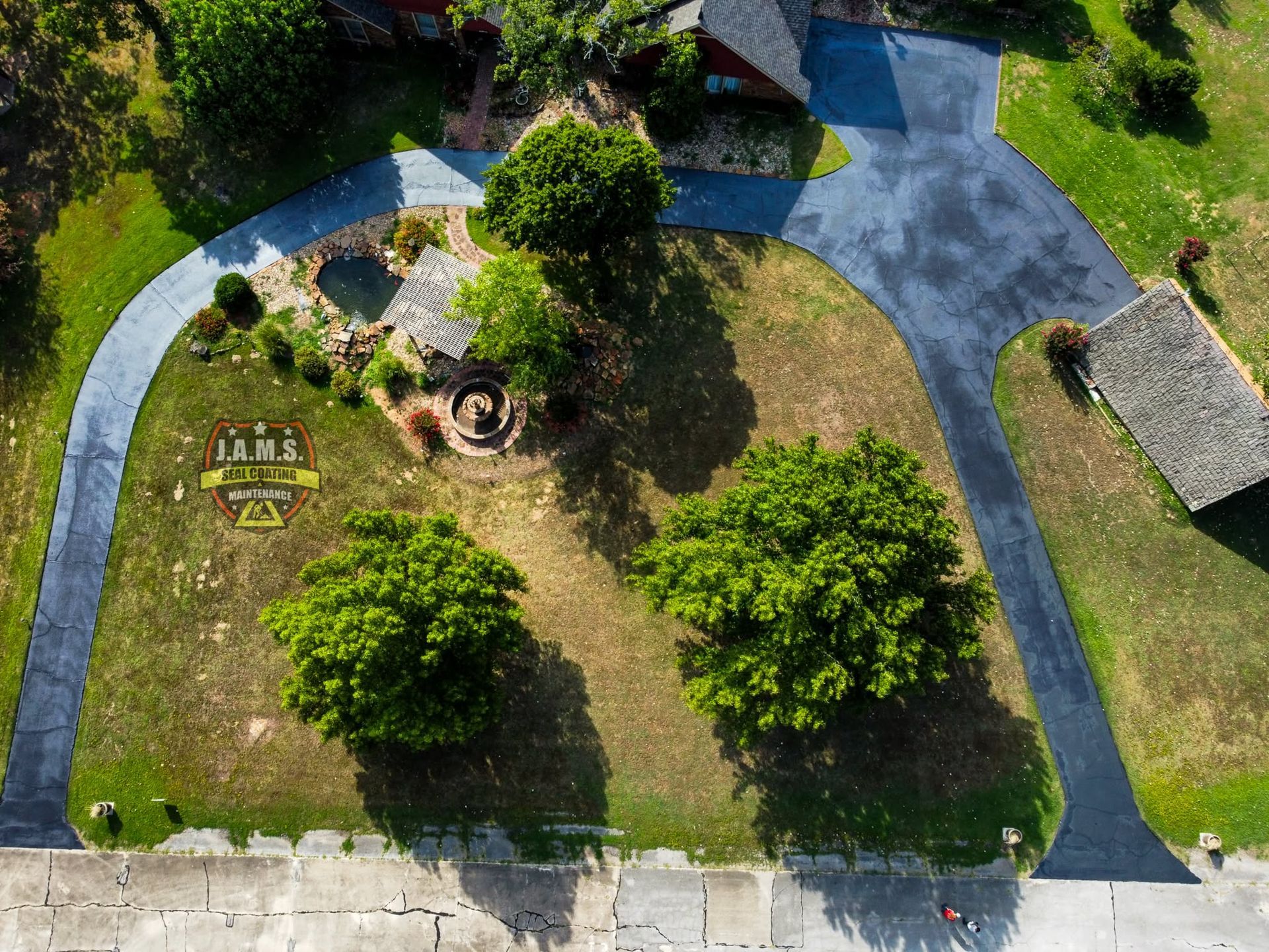 Aerial view of a park with winding paths, trees, grass, and a small gazebo area.