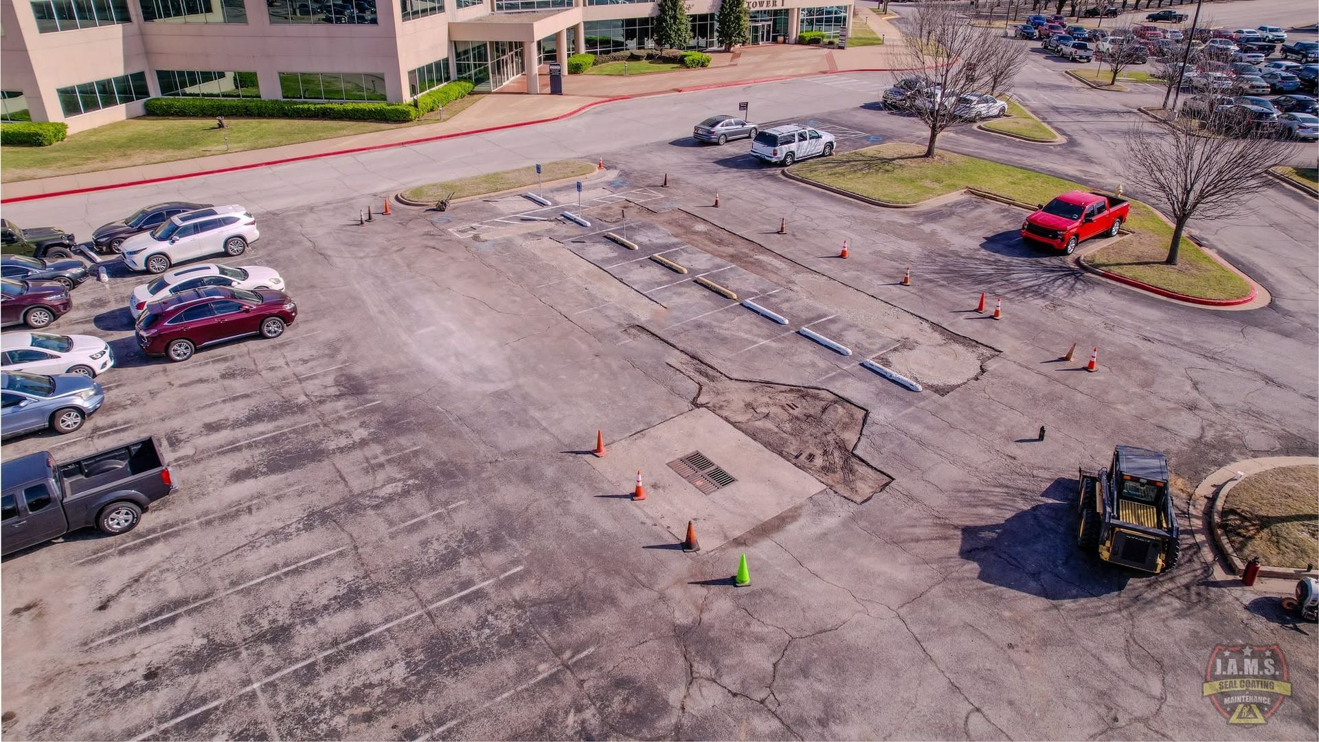 Aerial view of a parking lot under construction with equipment, cones, and marked paving areas