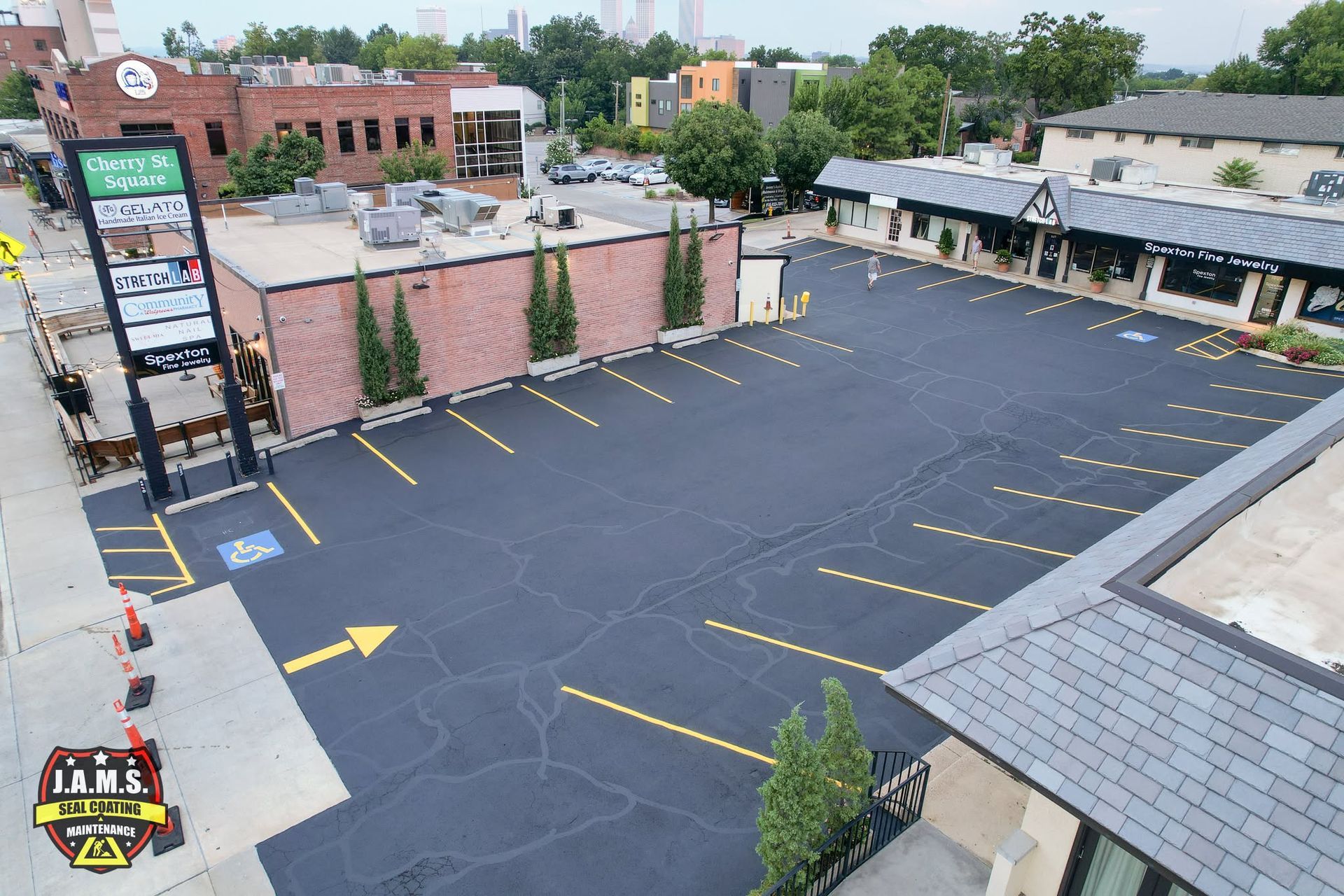 Empty paved parking lot beside brick and gray buildings, with yellow lines and arrows.