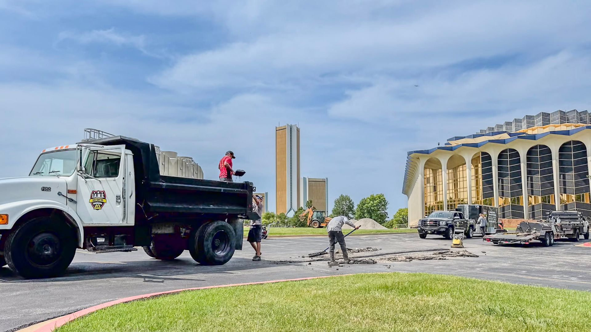 Dump truck and workers beside a grand building after an apparent incident, with debris on the pavement.