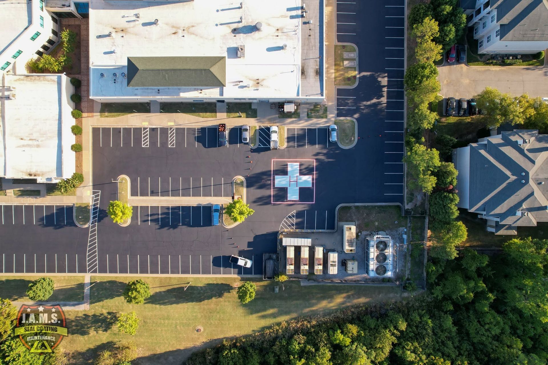 Aerial view of a building parking lot with marked spaces, vehicles, and trees around the lot.