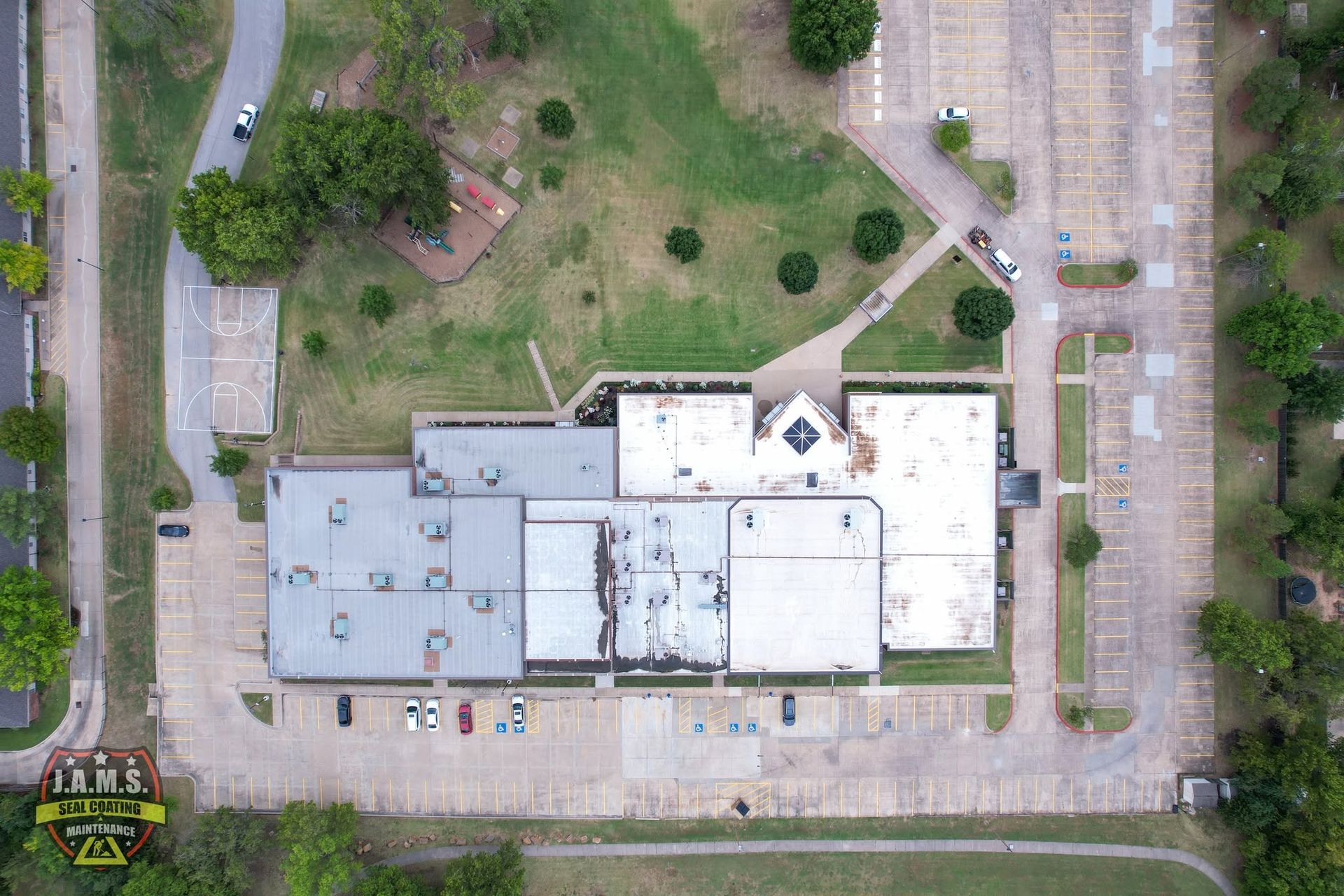 Aerial view of a single-story building with a parking lot, trees, and surrounding streets.
