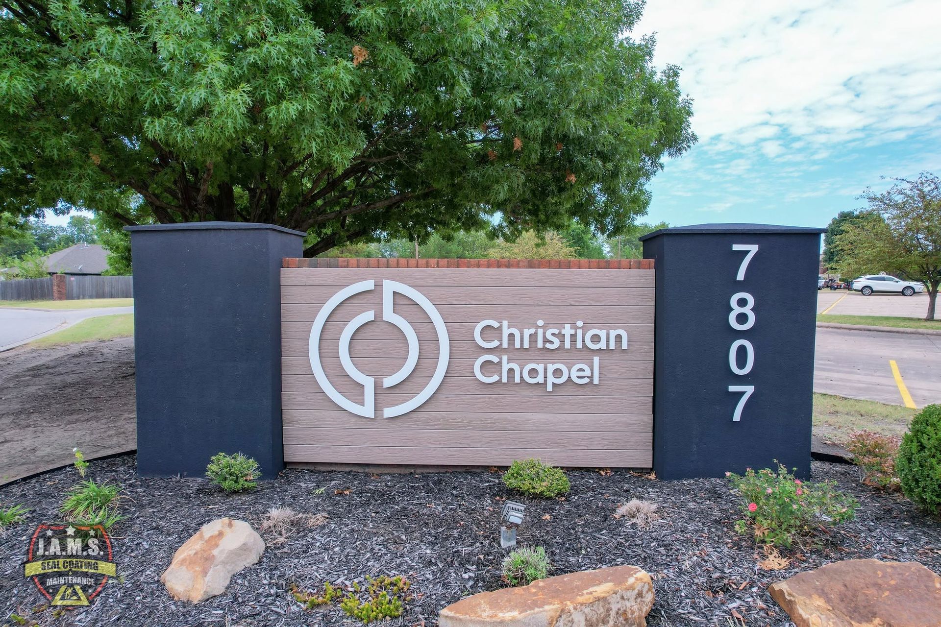Christian Chapel entrance sign with address 7807, set in front of trees and gravel landscaping