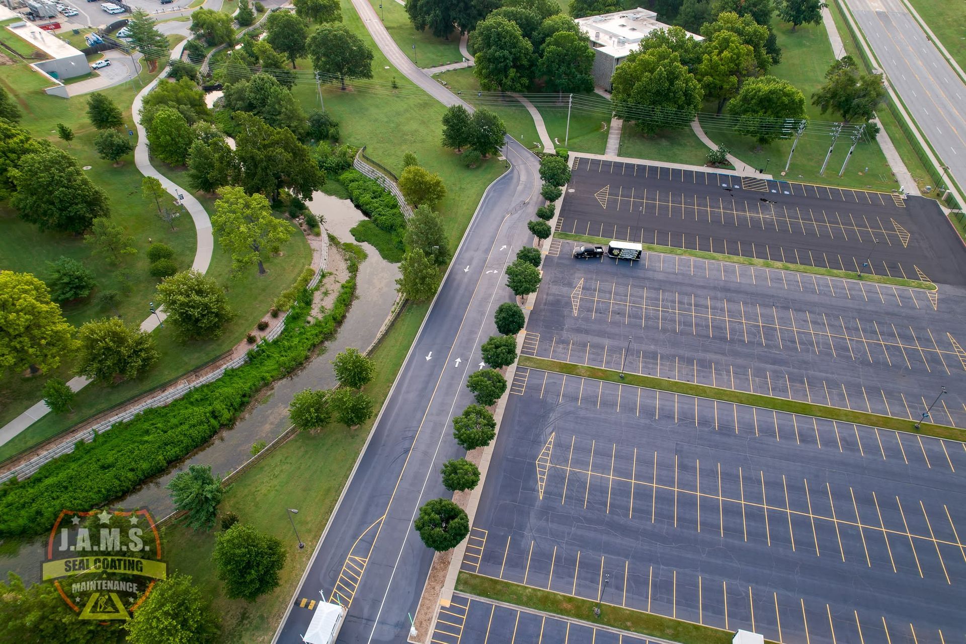Aerial view of an empty parking lot beside a tree-lined road and green parkland
