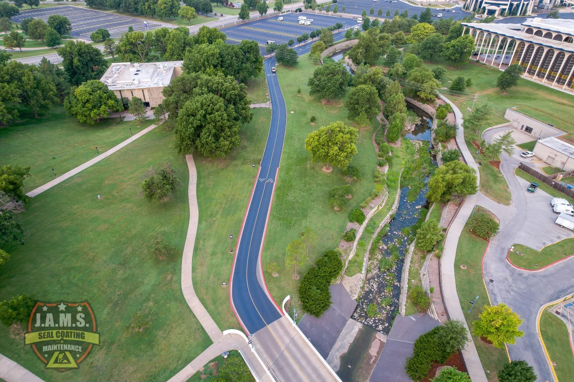 Aerial view of a winding blue path through a green park beside parking lots and buildings