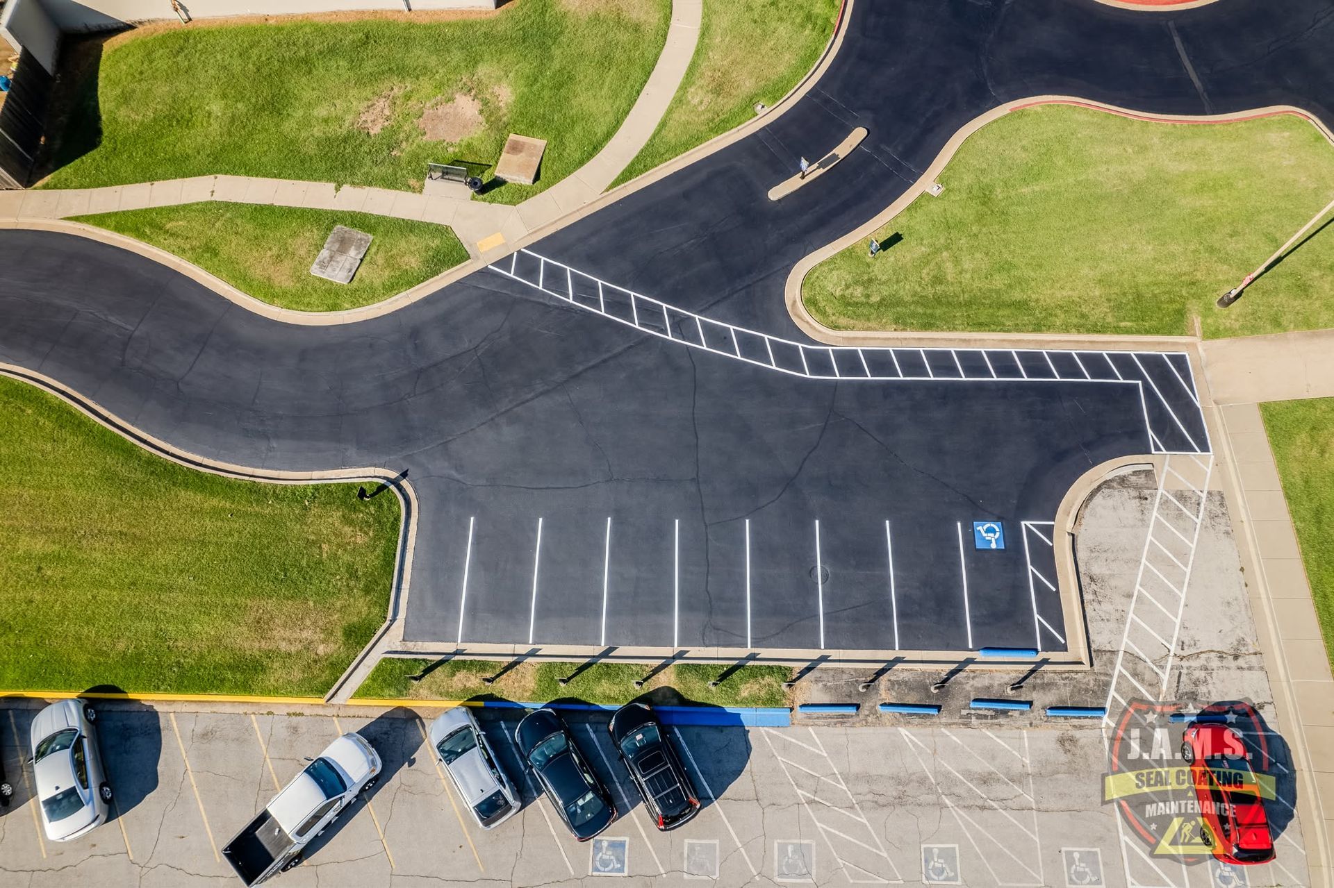 Aerial view of a mostly empty parking lot with several parked cars and surrounding grassy paths.
