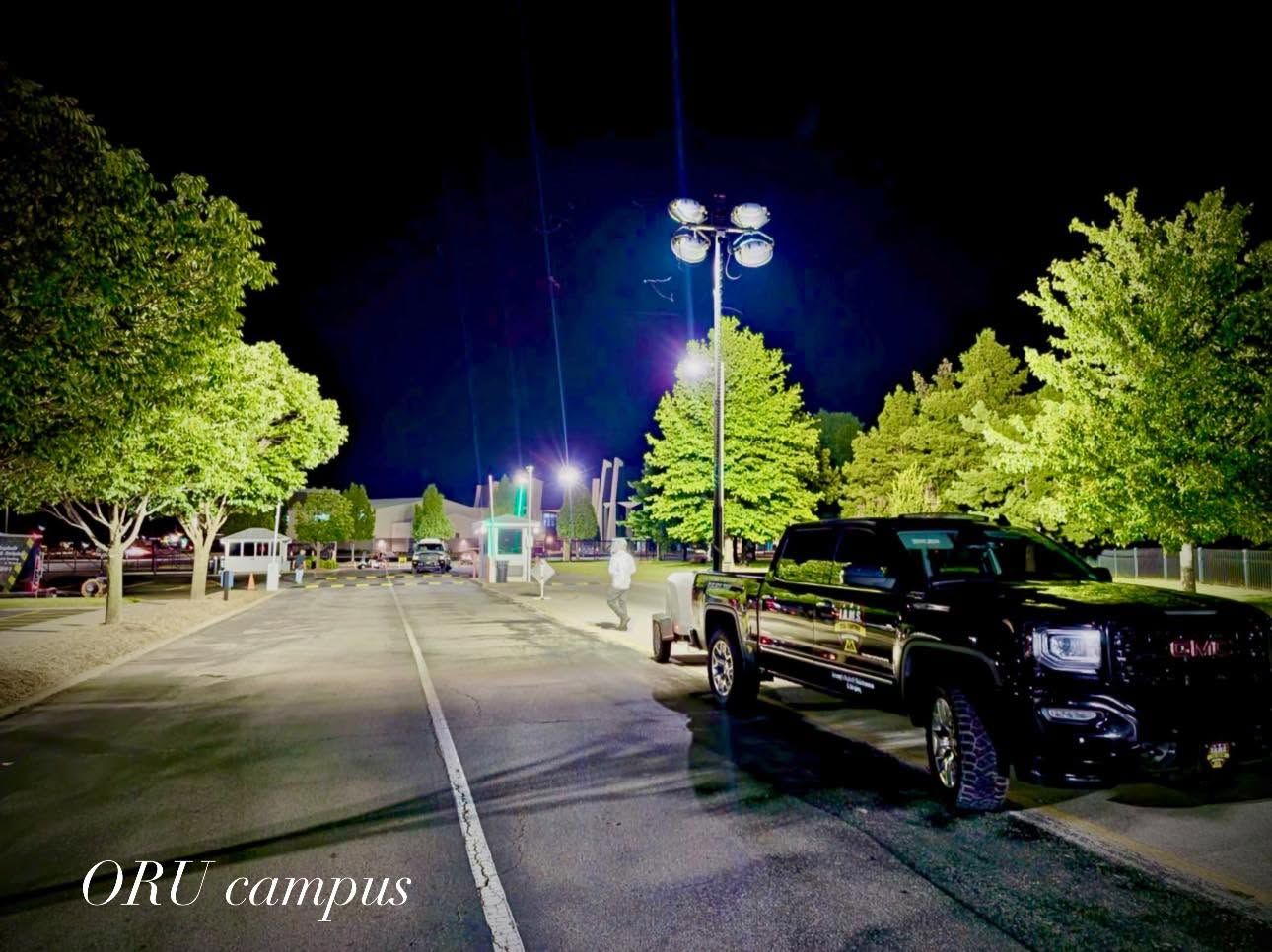 Nighttime campus road with parked trucks, trees, and bright streetlights