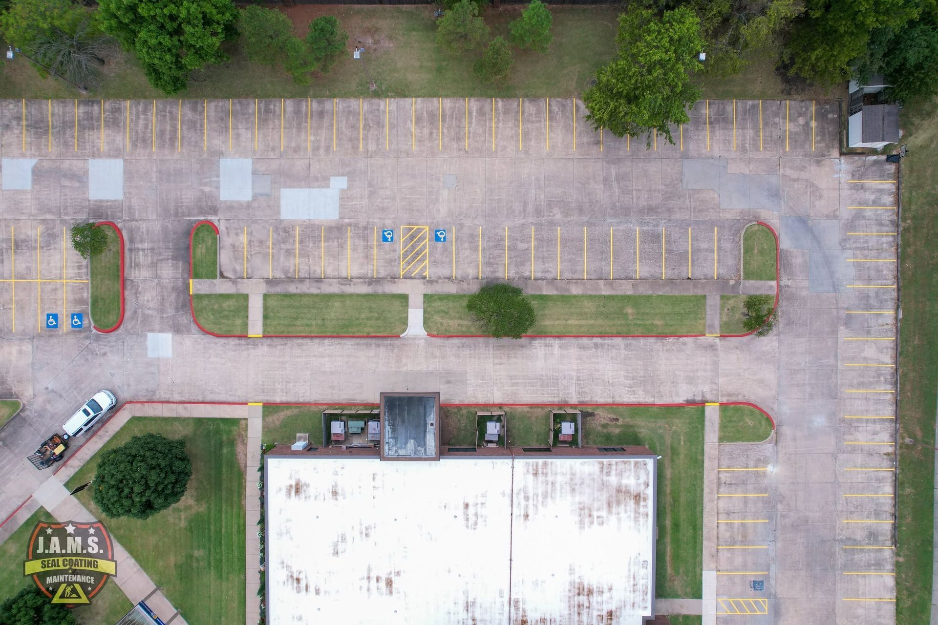 Aerial view of an empty parking lot with painted spaces, trees, and a building roof.