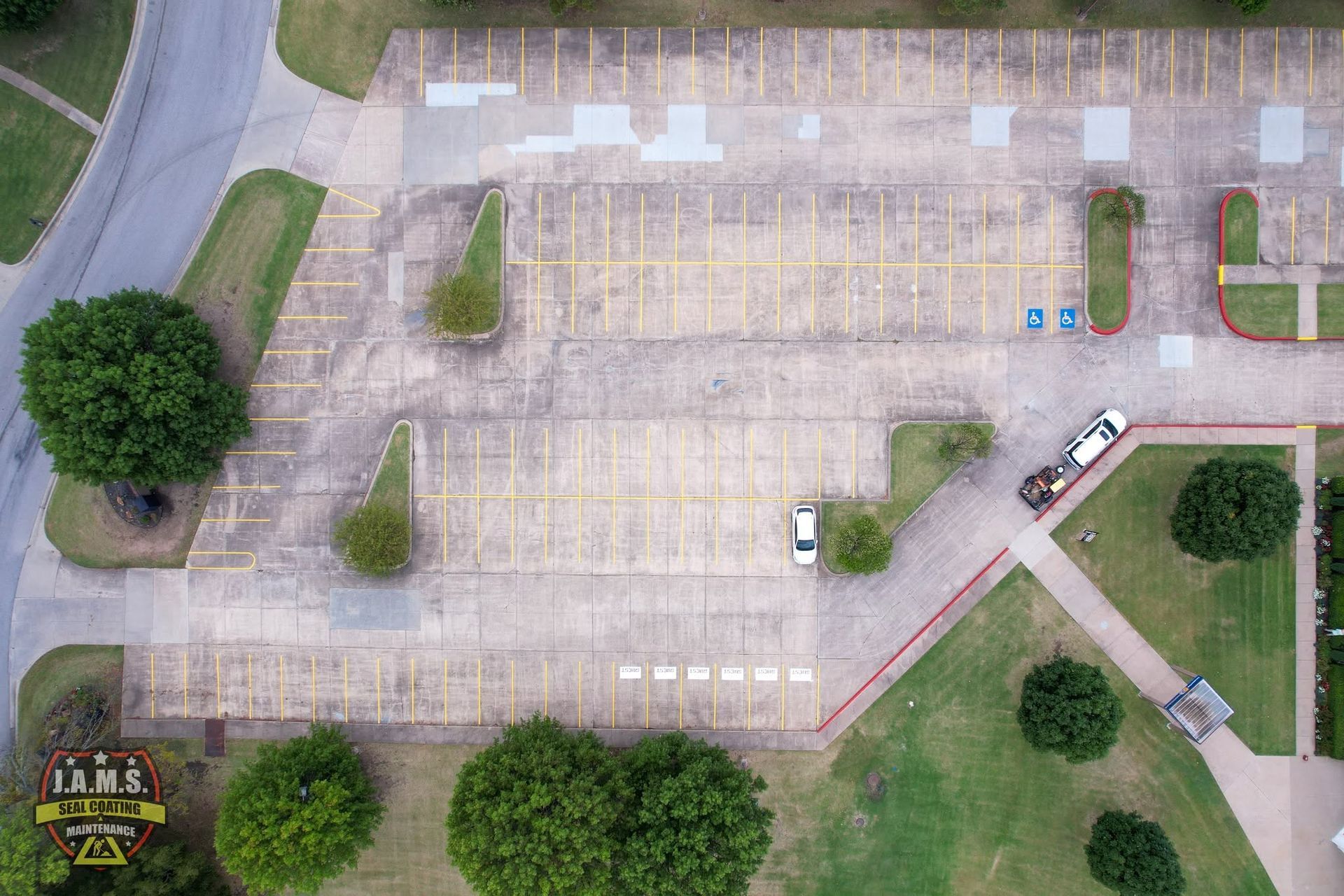 Aerial view of an empty parking lot with scattered trees and a few parked vehicles near the edges