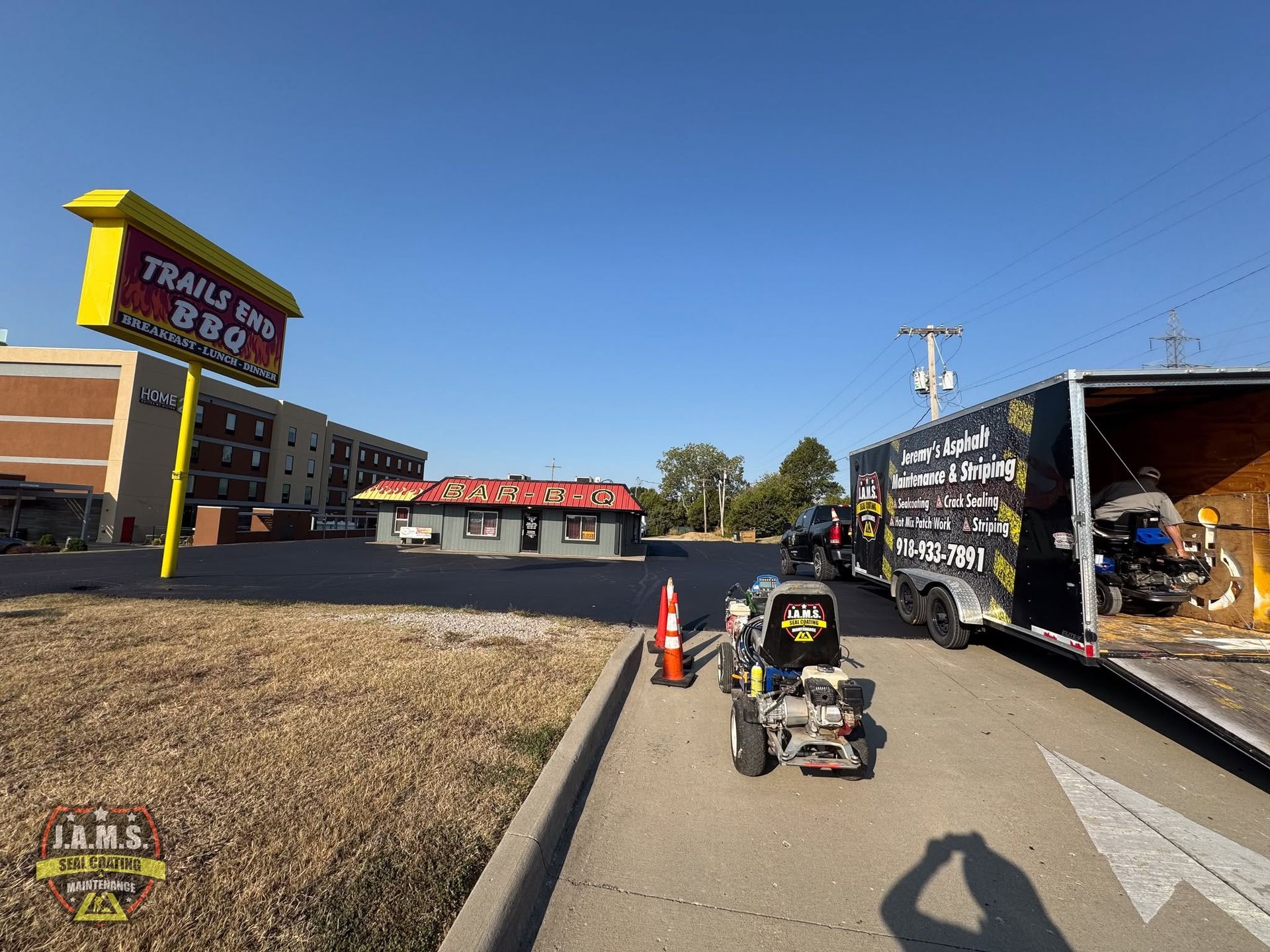 Person pushing a small cart past a trailer truck and storefront on a sunny roadside.