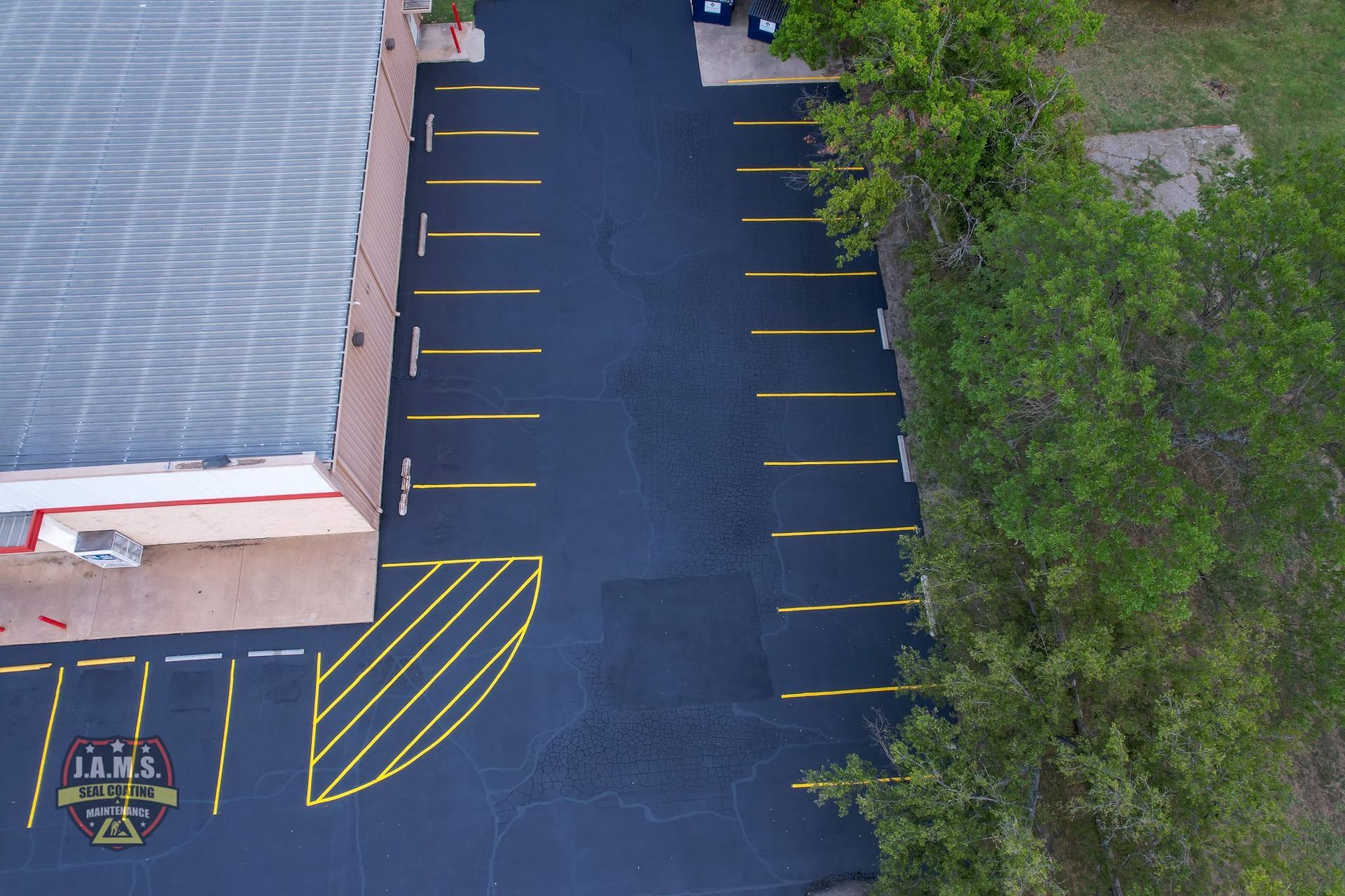Empty parking lot beside a building, with yellow parking lines and trees along the right side.