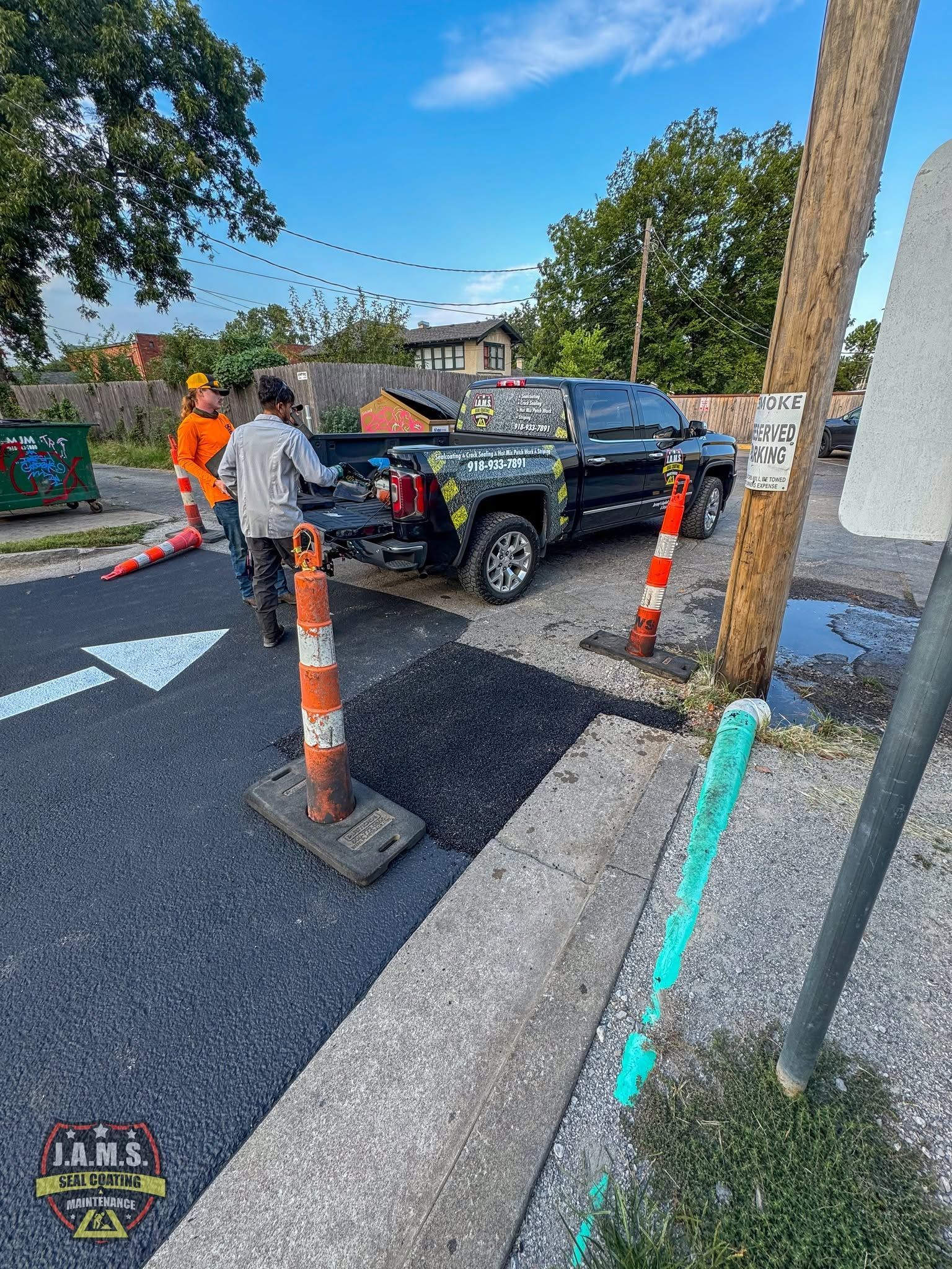 Roadwork crew painting lane markings beside a black pickup on a newly paved street with cones and barriers