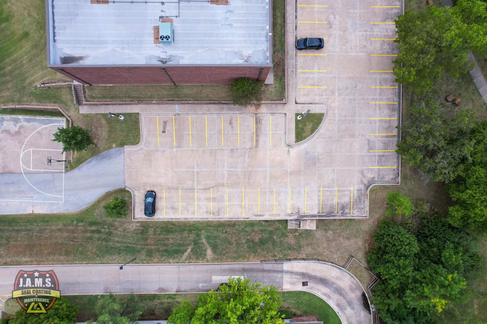 Aerial view of an empty parking lot beside a building and trees, with a few parked cars.
